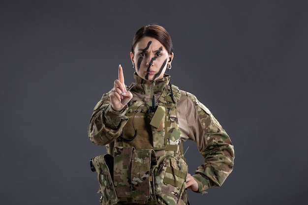 Vue de face d'une femme soldat en uniforme militaire sur un mur sombre