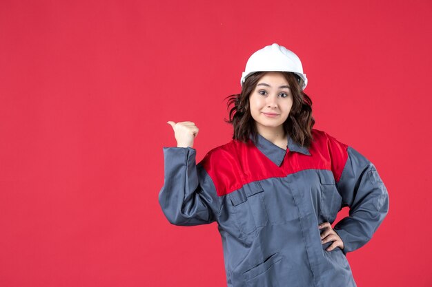 Vue de face d'une femme souriante en uniforme avec un casque et faisant un geste correct sur fond rouge isolé