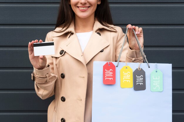 Vue de face de la femme tenant une carte de crédit et un sac à provisions avec des étiquettes de vente