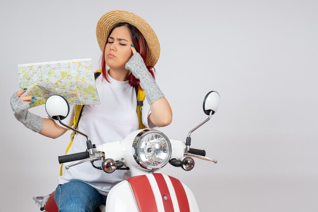 Vue de face femme touriste assise sur une moto avec mur blanc de carte