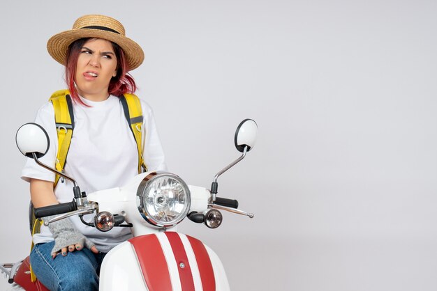 Vue de face femme touriste assise sur une moto sur un mur blanc