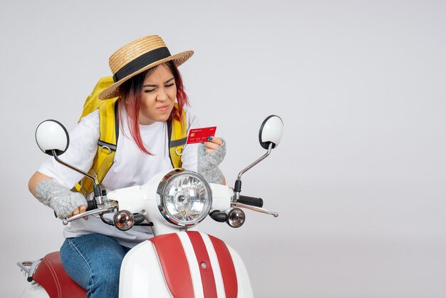 Vue de face femme touriste assise sur une moto tenant un mur blanc de carte bancaire