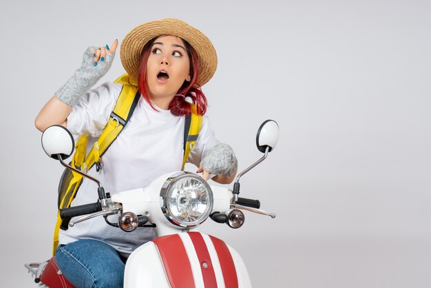 Vue de face femme touriste assise et posant sur une moto sur un mur blanc