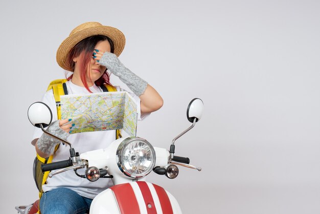 Vue de face femme touriste assise et posant sur une moto sur un mur blanc