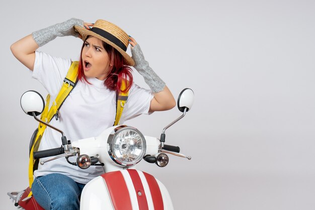 Vue de face femme touriste assise et posant sur une moto sur un mur blanc