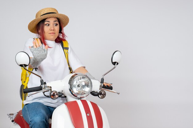 Vue de face femme touriste assise et posant sur une moto sur un mur blanc