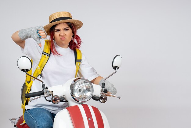 Vue de face femme touriste assise et posant sur une moto sur un mur blanc