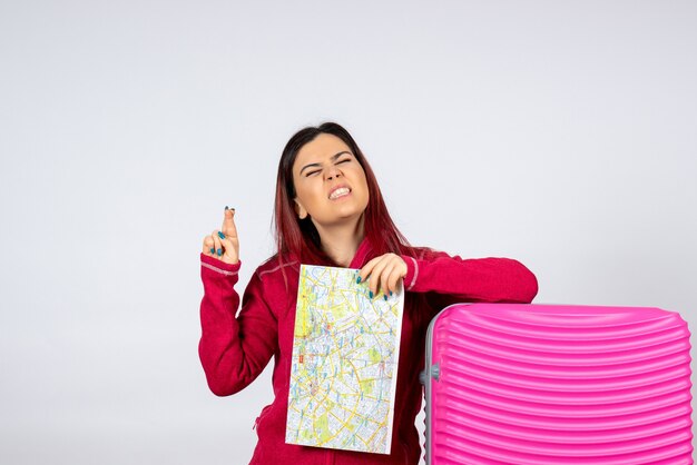 Vue de face femme touriste avec sac rose tenant la carte sur mur blanc