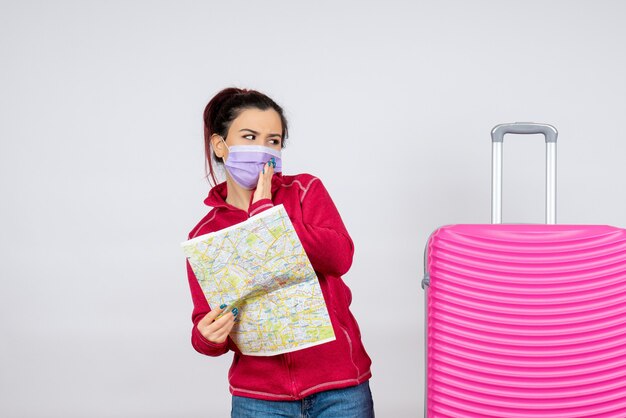Vue de face femme touriste tenant une carte en masque sur un mur blanc émotion de voyage covid- virus couleur pandémie de vacances