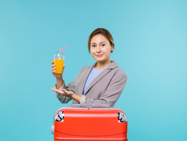 Vue de face femme en vacances avec son sac rouge tenant du jus de fruits frais sur le fond bleu vacances avion voyage mer voyage