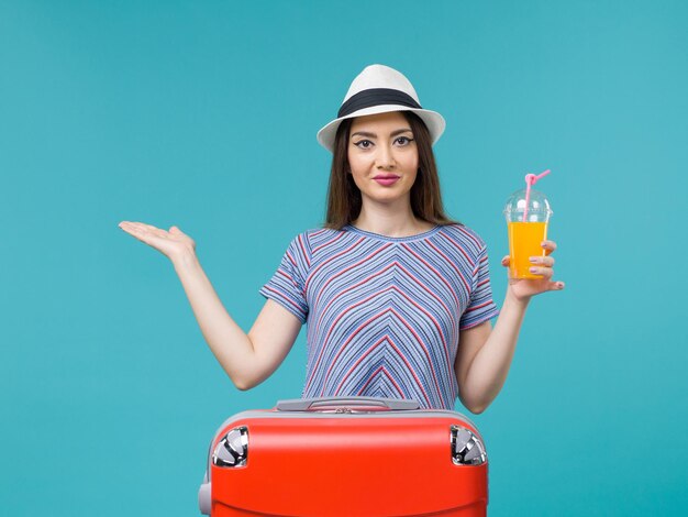 Vue de face femme en vacances avec son sac rouge tenant son jus sur le fond bleu voyage voyage vacances femme voyage