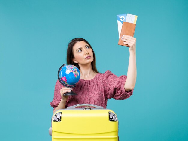 Vue de face femme en vacances tenant des billets d'avion et globe sur le fond bleu mer vacances femme voyage voyage été