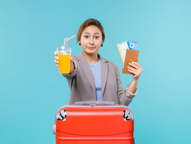 Vue de face femme en vacances tenant des jus de fruits frais et des billets sur le plancher bleu mer vacances avion voyage voyage voyage