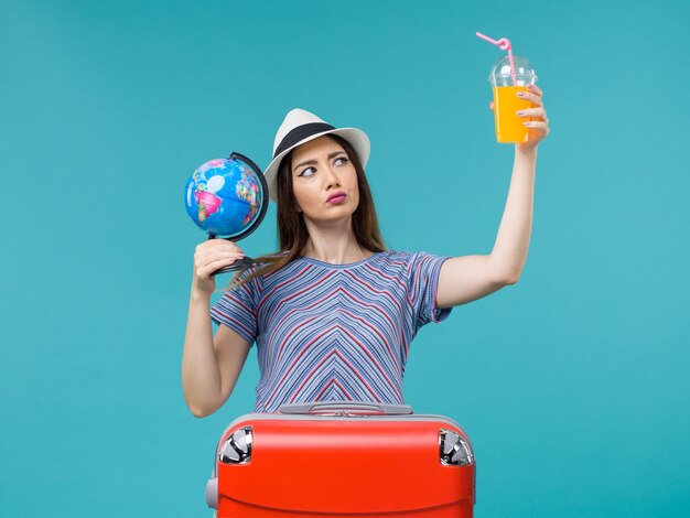 Vue de face femme en vacances tenant le jus et le globe sur le bureau bleu voyage en mer voyage vacances été