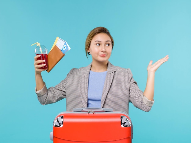 Vue de face femme en vacances tenant un verre de jus de fruits frais et des billets sur fond bleu clair voyage avion vacances voyage voyage mer