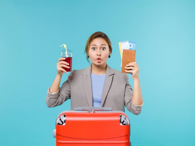 Vue de face femme en vacances tenant un verre de jus de fruits frais et billets sur fond bleu voyage voyage avion vacances voyage