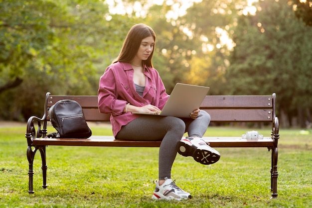 Vue de face femme vérifiant son ordinateur portable alors qu'il était assis sur le banc