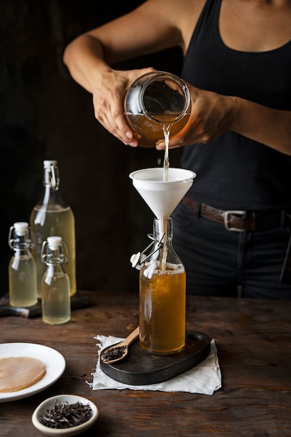 Photo gratuite vue de face femme versant du kombucha en bouteille