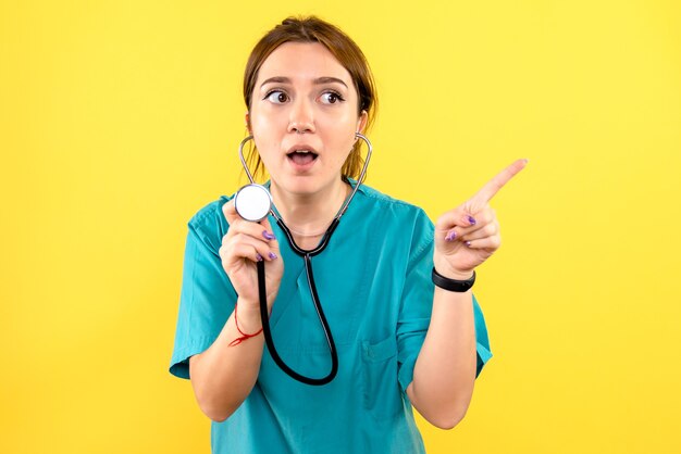 Vue de face de la femme vétérinaire à l'aide d'un stéthoscope sur mur jaune