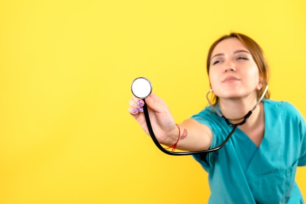 Vue de face de la femme vétérinaire à l'aide d'un stéthoscope sur mur jaune