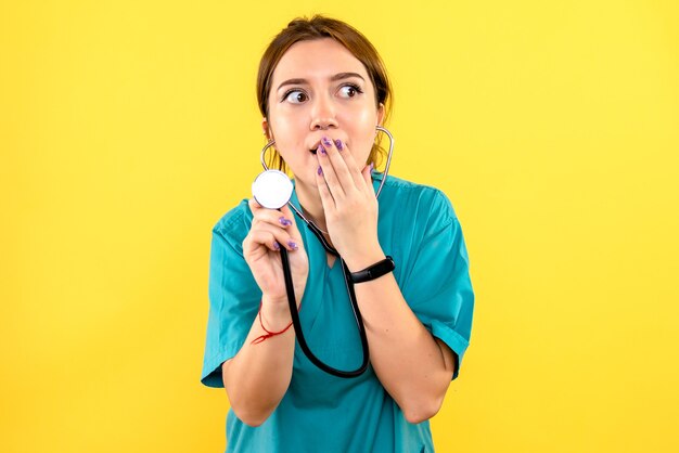 Vue de face de la femme vétérinaire à l'aide d'un stéthoscope sur mur jaune