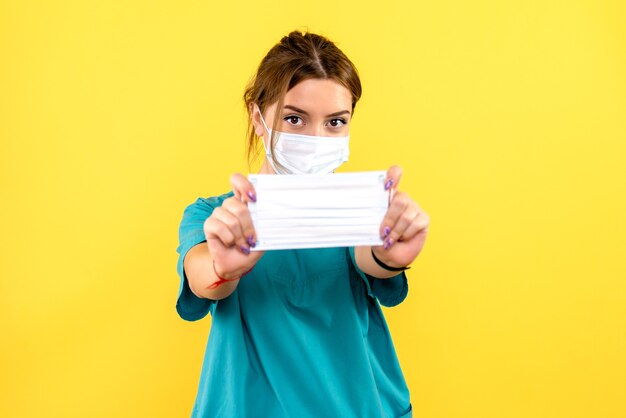 Vue de face de la femme vétérinaire avec masque sur mur jaune