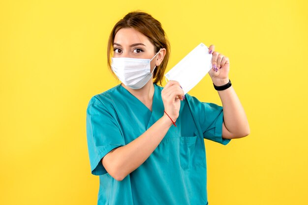 Vue de face de la femme vétérinaire avec masque sur mur jaune