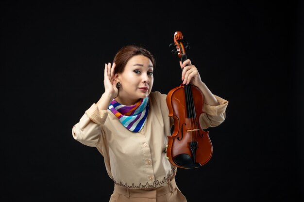 Vue de face femme violoniste tenant son violon écoutant sur un mur sombre