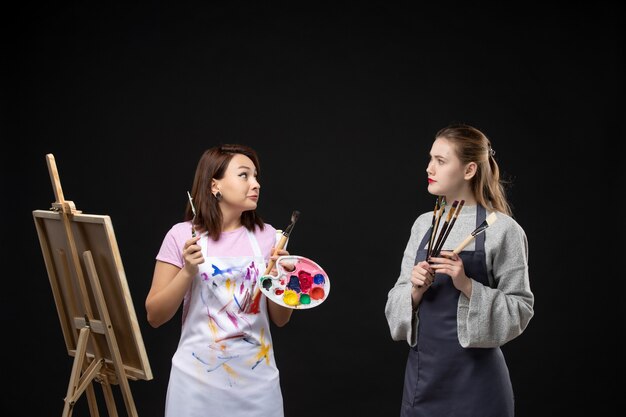 vue de face femmes peintres tenant des peintures et des glands pour dessiner sur le mur noir photo art artiste couleur travail photo dessiner peinture