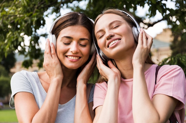 Vue de face des femmes souriantes à l'extérieur, écouter de la musique sur des écouteurs