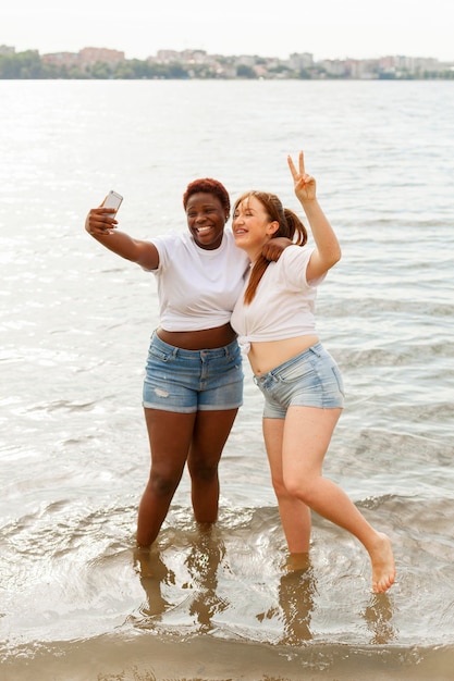 Vue de face des femmes souriantes prenant selfie à la plage
