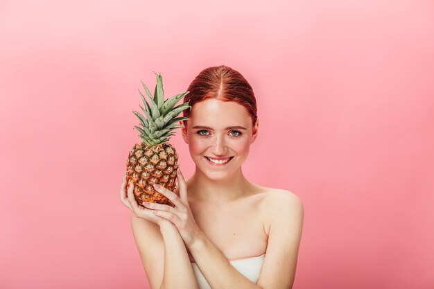 Vue de face d'une fille agréable avec des fruits exotiques. Photo de Studio de jeune femme au gingembre à l'ananas isolé sur fond rose.