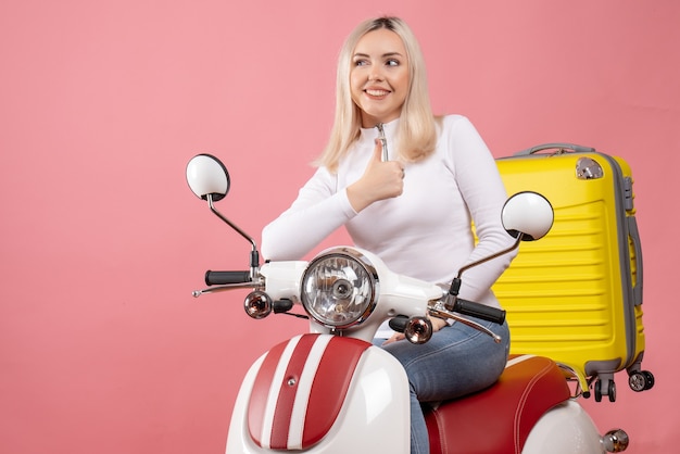 Vue de face fille blonde heureuse sur un cyclomoteur donnant les pouces vers le haut