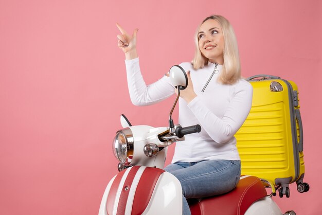 Vue de face fille blonde heureuse sur un cyclomoteur en montrant quelque chose