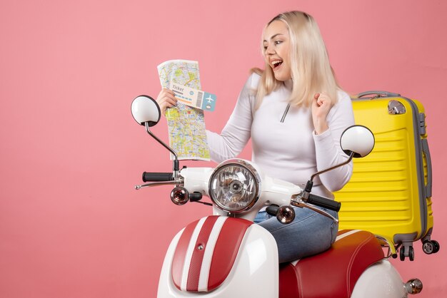 Vue de face fille blonde heureuse sur cyclomoteur tenant le billet et la carte