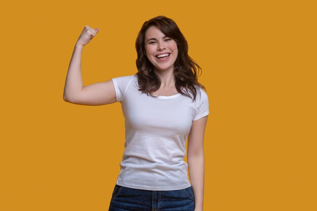 Vue de face d'une fille brune en forme souriante fléchissant les muscles de son bras devant la caméra