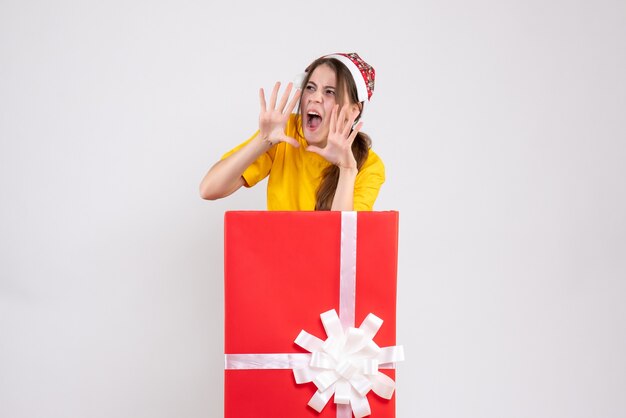 Vue de face fille en colère avec bonnet de Noel criant derrière gros cadeau de Noël