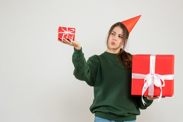 Vue de face fille curieuse avec chapeau de fête comparant ses cadeaux de Noël