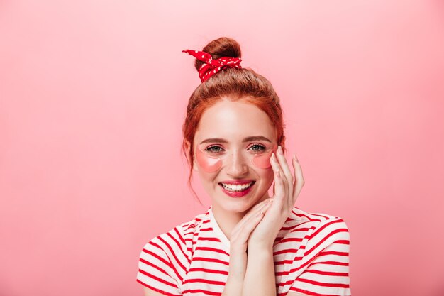 Vue de face d'une fille merveilleuse avec des patchs oculaires. Photo de Studio de charmante femme au gingembre faisant des soins de la peau avec un sourire sincère.