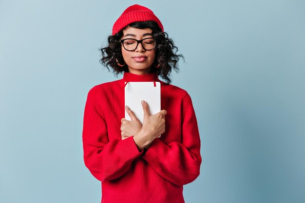 Vue de face d'une fille métisse aux yeux fermés Jolie jeune femme à lunettes et vêtements rouges debout sur fond bleu