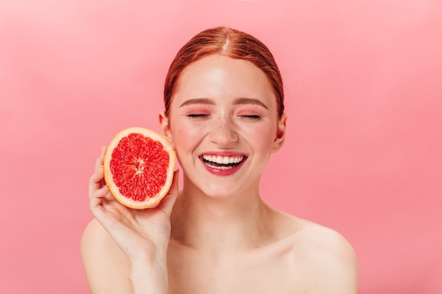 Vue de face d'une fille nue gaie avec pamplemousse frais. Photo de Studio d'une femme souriante au gingembre enthousiaste aux agrumes.