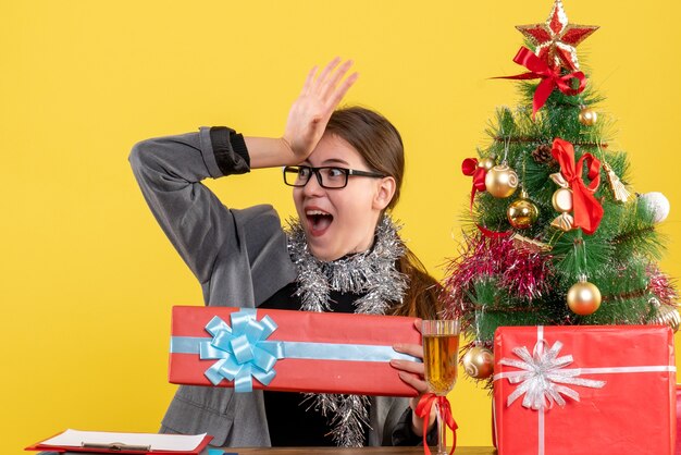 Vue de face fille perplexe avec des lunettes assis à la table mettant la main