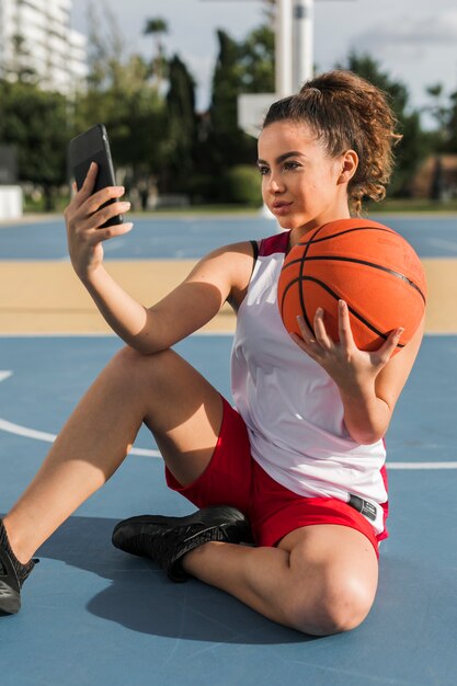 Vue de face de fille prenant selfie avec ballon de basket