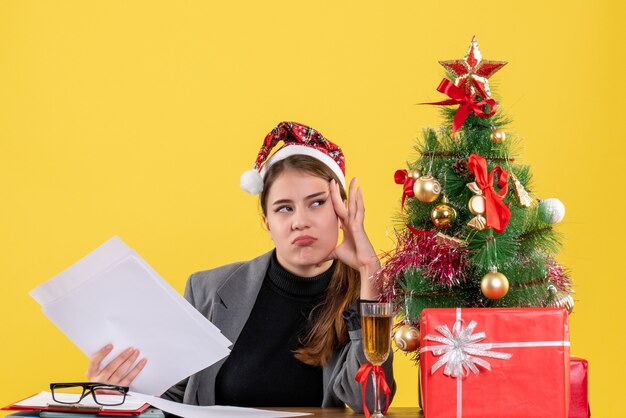 Vue de face fille réfléchie avec chapeau de Noël assis à la table mettant la main