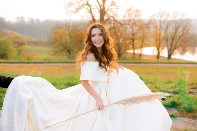 Vue de face d'une fille en robe blanche avec un épi de blé dans ses mains souriant dans le parc en automne