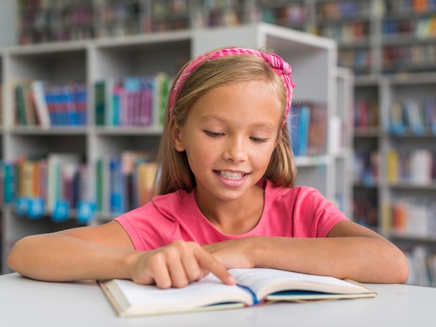 Vue de face, fille souriante, faire ses devoirs dans la bibliothèque