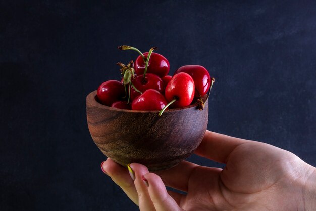 vue de face fille tient dans la main des cerises dans un bol en bois sur fond noir