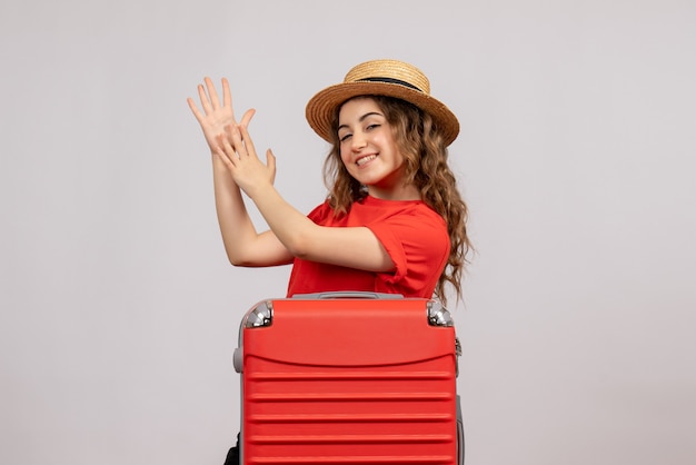 Vue de face de la fille de vacances avec sa valise applaudissant des mains debout sur un mur blanc
