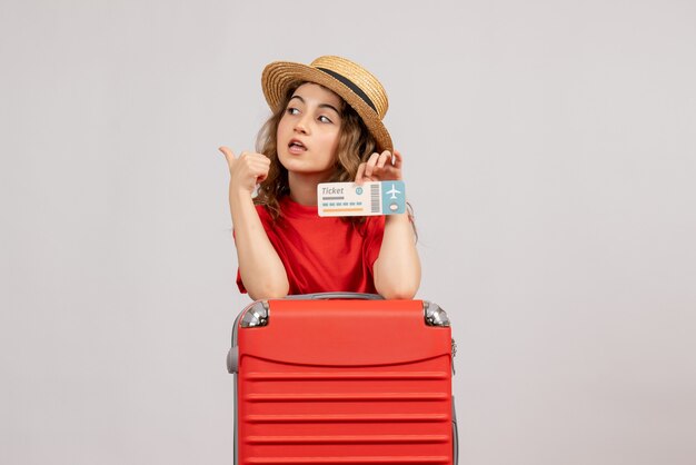 Vue de face de la fille de vacances avec sa valise tenant un billet faisant signe de pouce en l'air