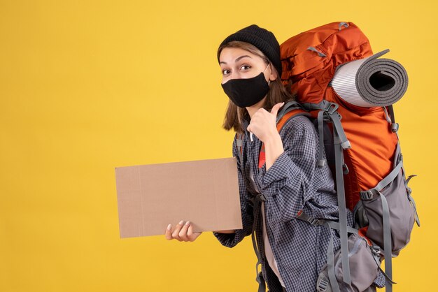 Vue de face de la fille de voyageur heureux avec masque noir et sac à dos tenant carton